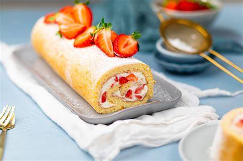Angerichtete Biskuitrolle mit Buttercreme und Erdbeeren im Anschnitt mit fruchtiger Dekoration