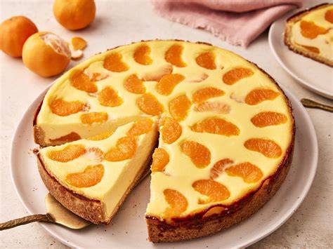Angeschnittener Mandarinen-Quarkkuchen auf einer Glasplatte mit Deko-Mandarinen