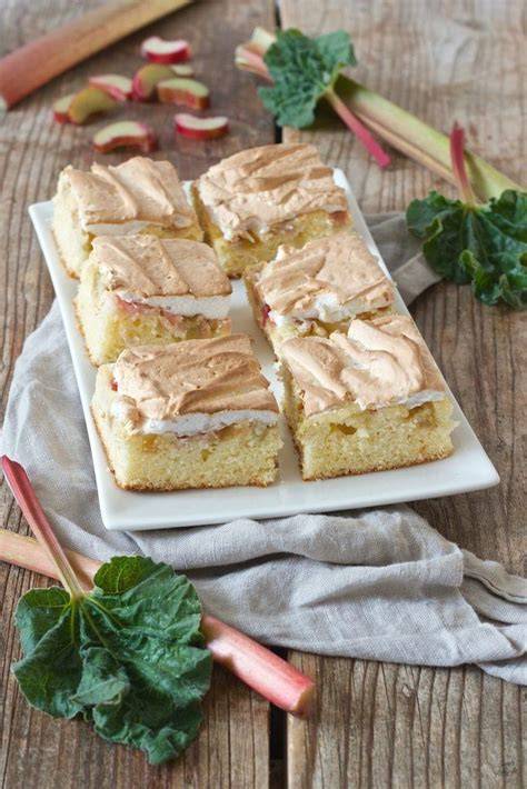 Angeschnittener Rhabarberkuchen mit Baiserhaube auf einem holzernen Tisch, Backblech im Hintergrund