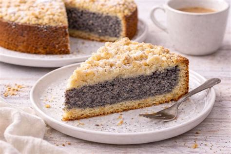 Anrichten: Stück Mohnkuchen auf Teller, Zitronenguss glänzend, daneben Tasse Kaffee