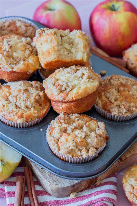 Apfel-Streusel-Muffins auf einem Holzbrett, Äpfel und Zutaten arrangiert