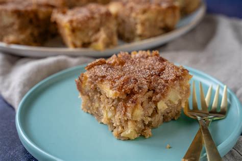 Apfelkuchen mit kleinen Apfelstücken auf rustikalem Holzbrett, Zimt und Zucker daneben