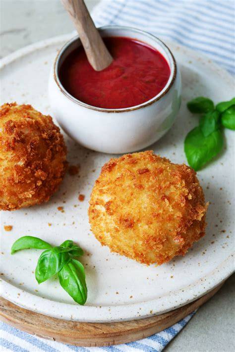 Arancini auf Teller serviert mit frischer Tomatensauce und Basilikum