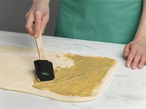 Arbeitsfläche mit dünn ausgerollten Teigfladen und Butter verstreichen