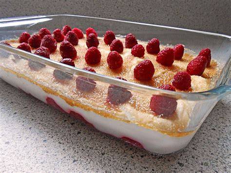 Auflaufform mit geschichteten Himbeeren und Joghurt-Creme, bestreut mit braunem Zucker