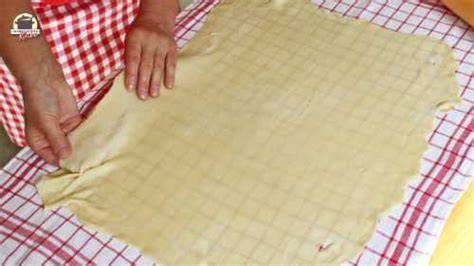 Ausgerollter Strudelteig auf bemehltem Leinentuch mit ausgestreckten Händen