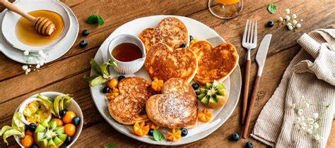 Auswahl an Pancakes, Rührei und frischem Kuchen auf einem Holztisch