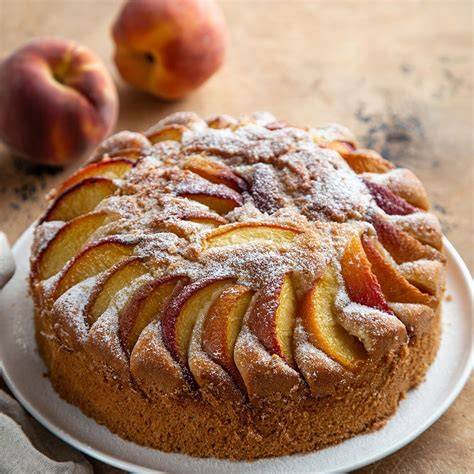 Backblech mit gebackenem Pfirsichkuchen in der Küche, Dosenpfirsiche und Zutaten im Hintergrund