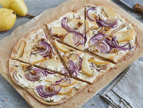 Belegte Flammkuchen vor dem Backen, Zutaten sichtbar: Ziegenkäse, Birne, rote Zwiebel, Thymian