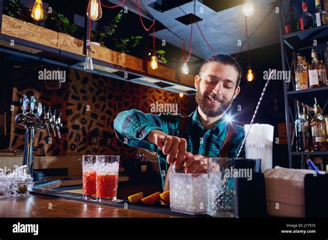 Beleuchtete Bar mit Cocktailgläsern und Barkeeper bei der Arbeit