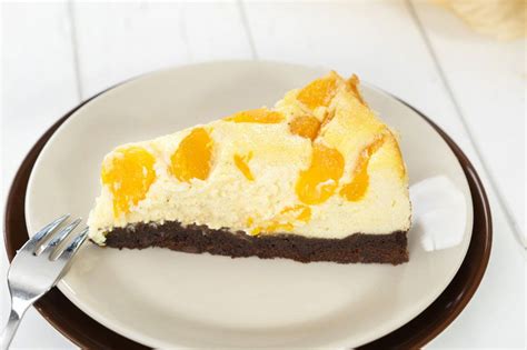 Brownie-Käsekuchen mit Mandarinen - angeschnitten, verschiedene Schichten deutlich sichtbar
