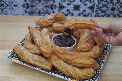 Churros mit Schokosauce und Puderzucker auf Holzbrett