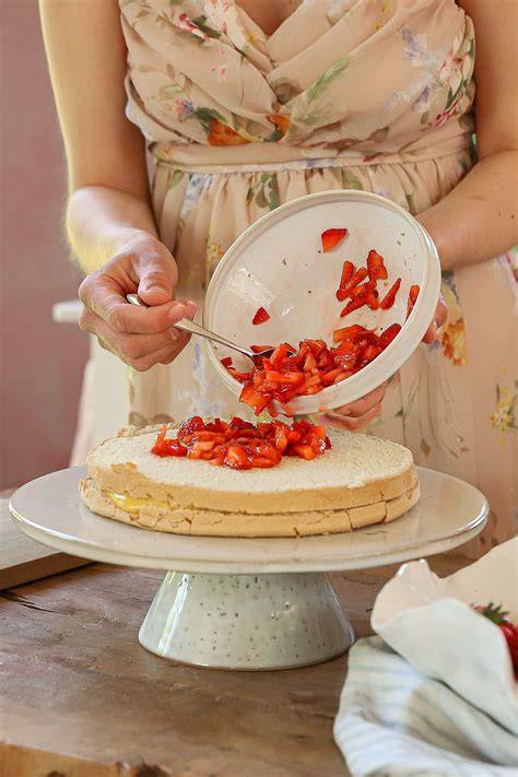 Cremeschichten und Erdbeeren werden auf Tortenboden verteilt