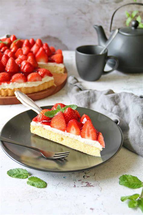 Ein Stück Kühlschranktorte auf einer Kuchengabel, im Hintergrund frische Erdbeeren und Keksboden