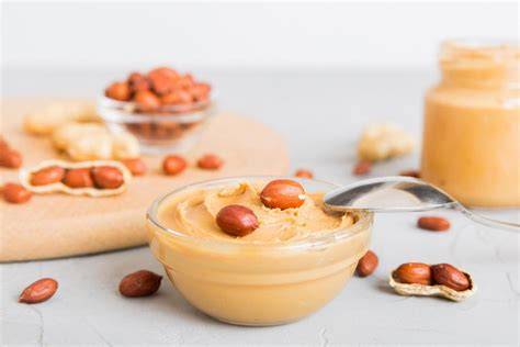 Eine Schüssel selbstgemachte Erdnussbutter, daneben frische Erdnüsse und ein Mixer