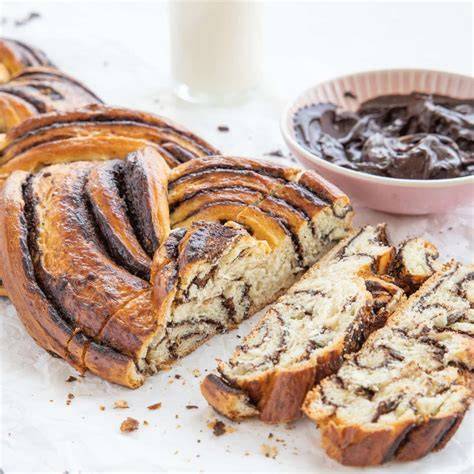 Fertig gebackener und glasierter Schoko-Hefezopf, angerichtet mit Puderzucker und Haselnüssen