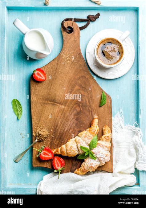 Frisch gebackene Croissants auf einem Holzbrett mit Marmelade und Kaffee