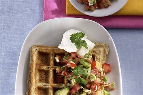 Frisch gebackene herzhafte Waffeln mit Avocado, belegt mit Ei, Tomate und Kräutern