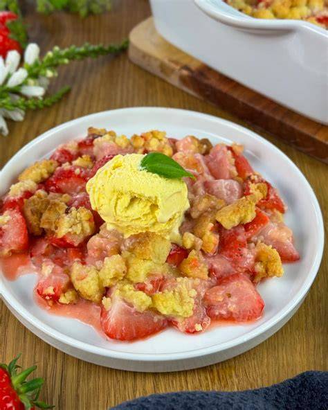 Frisch gebackener Erdbeer-Crumble mit Vanilleeis, goldbraune Streusel, serviert in Auflaufform