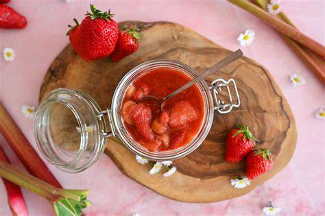 Frische Erdbeeren und Rhabarber auf einem Holzbrett, daneben Marmeladengläser