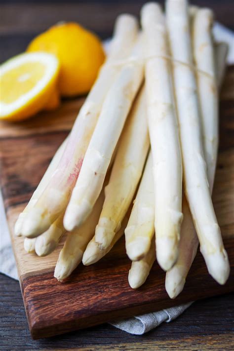 Frischer weißer Spargel auf einem Holztisch, daneben Spargelschäler und Zitrone