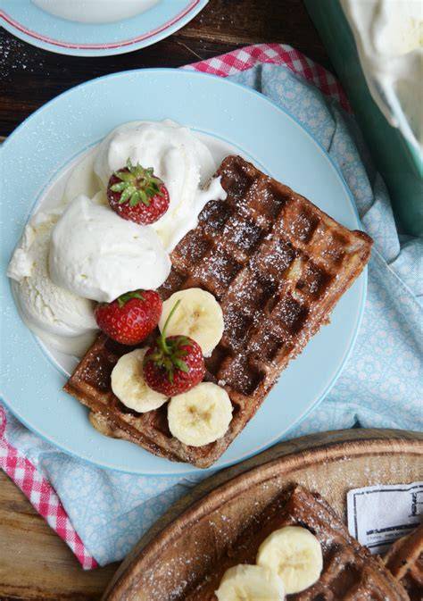 Gebackene Waffeln mit Vanilleeis und Erdbeeren auf Teller angerichtet