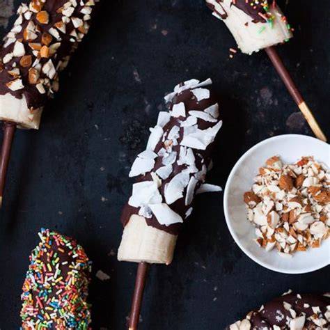 Gefrorene Schoko-Bananen auf Holzspießen mit bunten Toppings