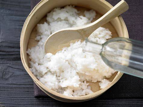 Gekochter Sushi-Reis in einer Schüssel, Reisessig wird eingerührt