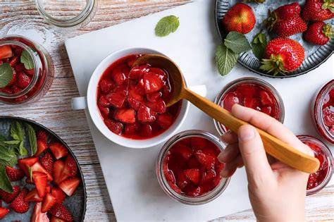 Gläser Erdbeer-Honig, frische Erdbeeren, Honiglöffel und Bienenwaben