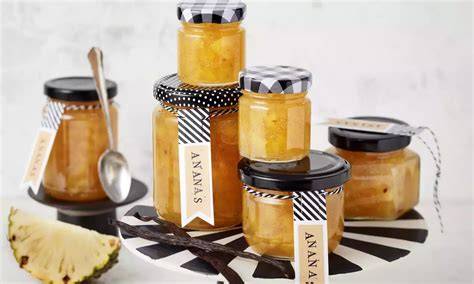 Gläser mit Ananasmarmelade, Dosenananas und Gelierzucker auf einer Arbeitsfläche
