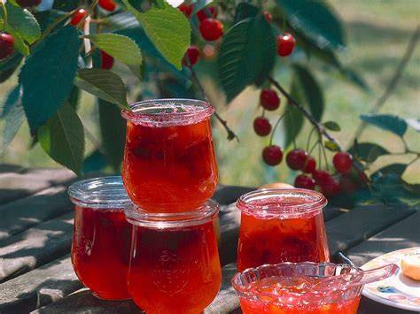 Gläser mit frisch eingekochter Kirsch-Orangen-Marmelade auf einem rustikalen Holztisch