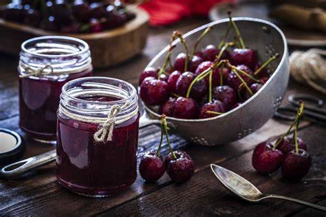 Gläser mit frischgekochter Kirsch-Zitronen-Marmelade auf einem Holzbrett