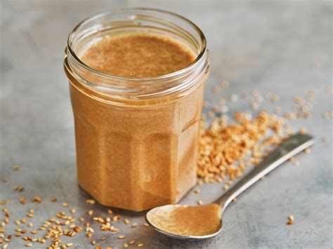 Glas Tahini-Schoko-Creme neben Rohkakao, Ahornsirup und Sesamsamen