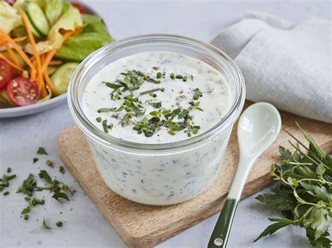 Glas mit Dressing auf Küchenwaage und Kräuter daneben
