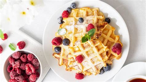 Goldbraune Protein-Waffeln mit Hüttenkäse auf einem Teller, daneben Beeren und Joghurt