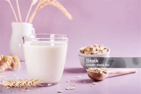 Hafermilch in Glas auf Holzuntergrund, daneben Haferflocken