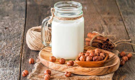 Haselnussmilch im Glas neben ganzen Haselnüssen und Müsli