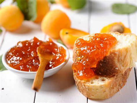 Hausgemachte Aprikosenmarmelade auf Brot, umgeben von frischen Aprikosen