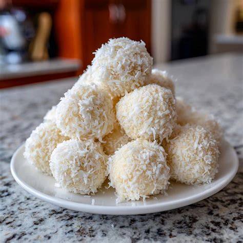 Hausgemachte Raffaello-Kugeln auf einem weißen Teller, umgeben von Kokosraspeln und Mandeln