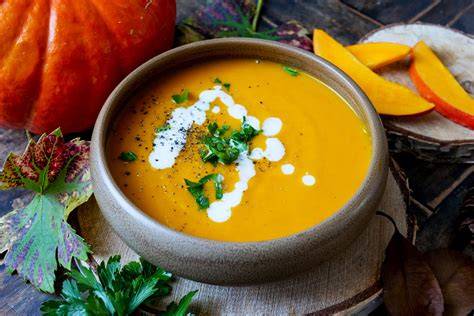 Herbstliche Kürbissuppe in einer Schale mit Toppings und Brotchips, im Hintergrund Herbstlaub