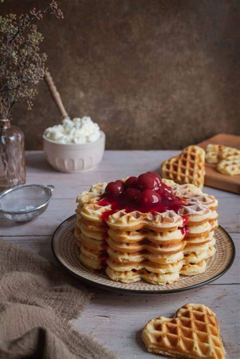 Herzwaffeln auf Gitter, bestäubt mit Puderzucker, mit heißen Kirschen
