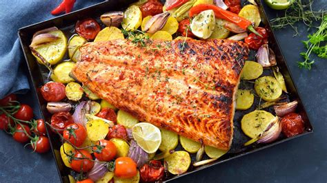 Honig-Senf-Lachs mit Ofengemüse auf Blech, angerichtet mit Zitronenscheiben und frischen Kräutern
