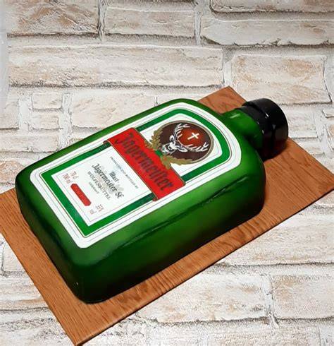 Jägermeister Torte angerichtet auf rustikalem Holzbrett, Flasche und Kräuter im Hintergrund