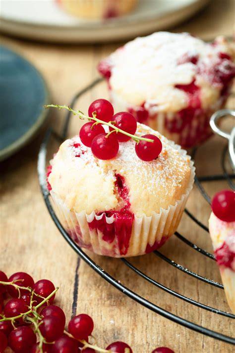 Johannisbeer-Muffins und Käsekuchen-Muffins auf einer sommerlichen Tafel, Zutaten angeordnet