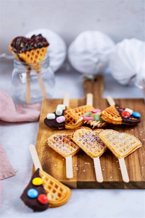 Kinder verziert bunte Waffel-Herzen mit Schokoguss und Streuseln