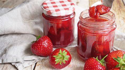 Kleine Gläser mit veganer Erdbeermarmelade, daneben Zutaten wie Chia, Zitrone und Vanille