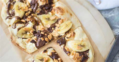 Knuspriger süßer Flammkuchen mit Schokocreme, Banane und Mandeln auf Holzbrett