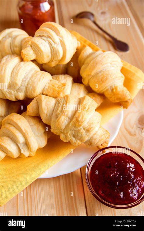 Korb mit frisch gebackenen Mini-Croissants auf einem Holztisch, Kaffee und Marmelade im Hintergrund