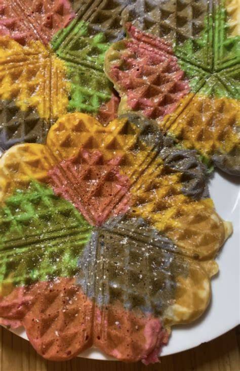 Kreativ angerichtete Regenbogenwaffeln in Herzform mit Zuckerdekor und Obstbeilage