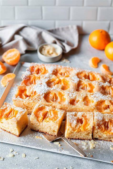 Mandarinenkuchen ohne Zucker angerichtet auf einem Holztisch - frische Mandarinen im Hintergrund
